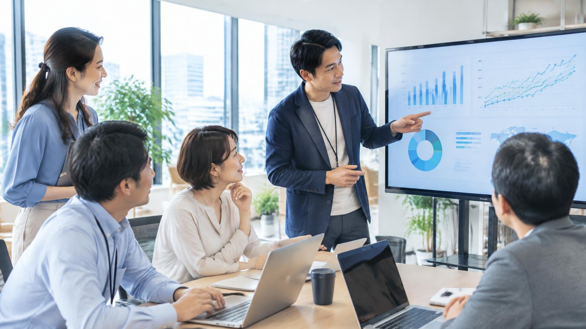 Team of Japanese office workers discussing data on a screen in a modern office